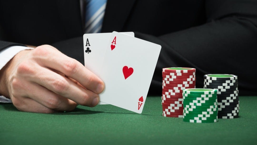 A poker player reveals his two aces next to a stack of poker chips.