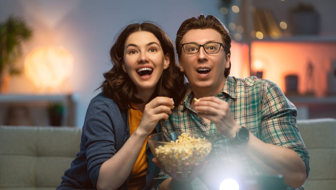 An excited couple eating popcorn while watching TV.