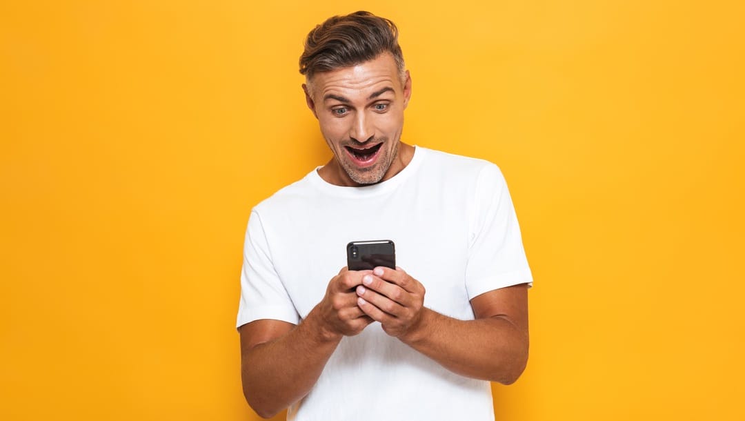 A man looking excitedly at his smartphone against a yellow background.