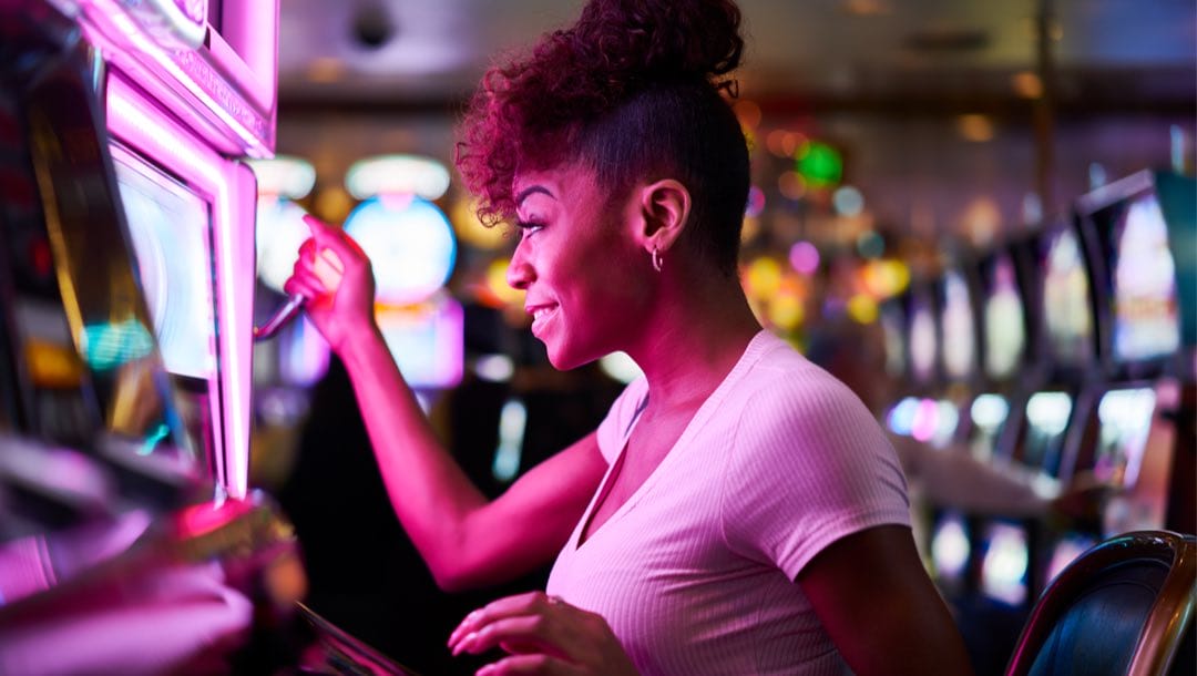 A woman pulling the lever of a slot machine in a casino.