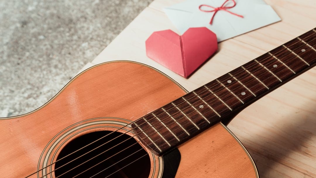 A guitar on a table with an origami heart and a letter next to it.