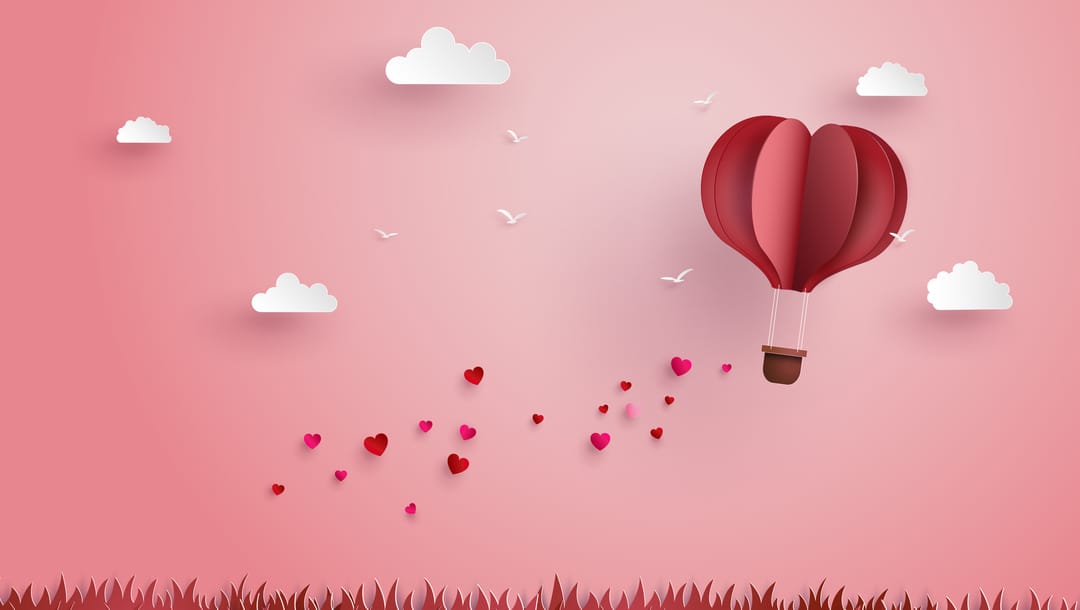 An origami hot air balloon with birds, clouds, hearts and grass on a pink background.