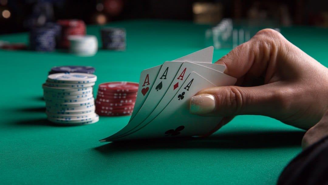 A woman holding a poker hand at the table with casino chips in the background.