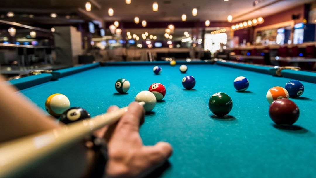 Players perspective of a cue aiming at a ball on a billiards table.