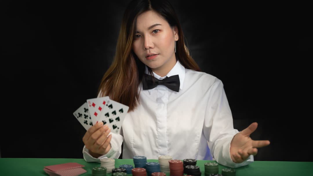 A woman standing at a poker table with cards in her hand and chips on the table.