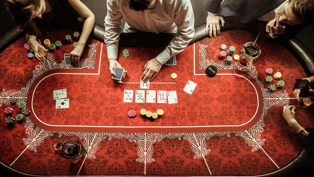 A high angle view of people playing poker at an oval-shaped table with red felt.