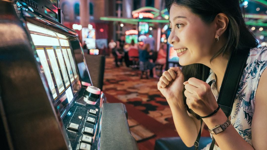 A woman clenches her hands in excitement while playing slots.