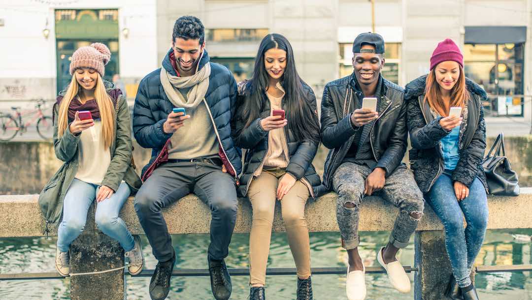 A group of people sitting outside playing on their mobile phones.