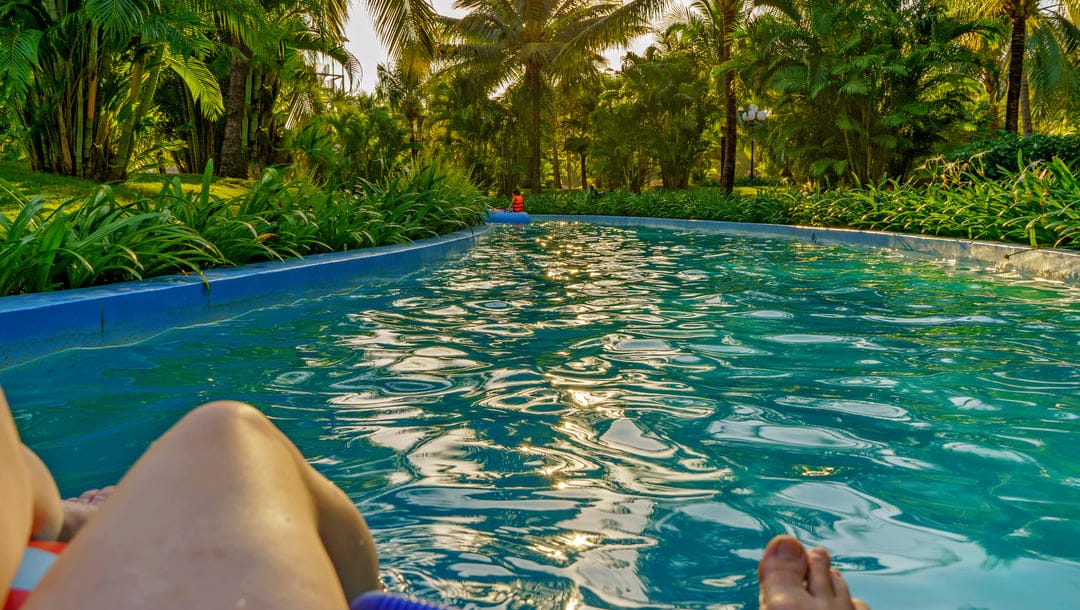 A person floats on a tube down a lazy river surrounded by greenery