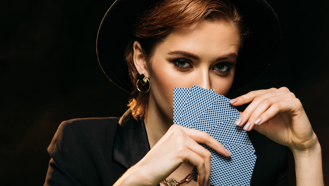 A woman uses cards to cover her mouth on a black background.