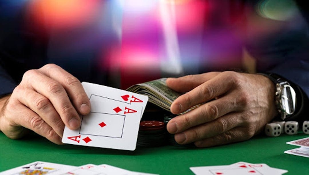 Poker player holding a pair of aces and money at a table with colorful lights in the background