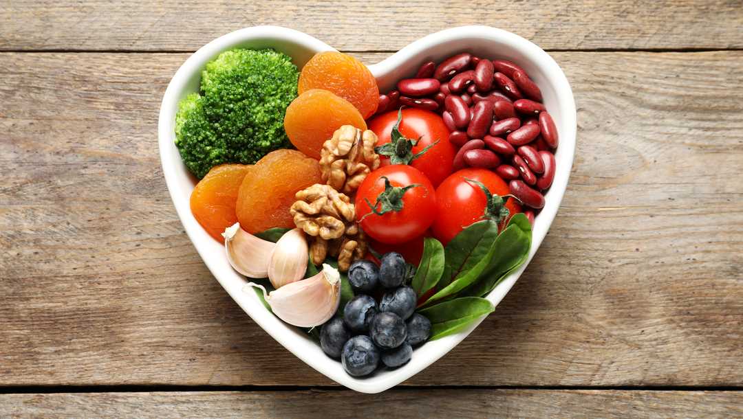 A heart-shaped bowl filled with beans, nuts, fruit and vegetables.