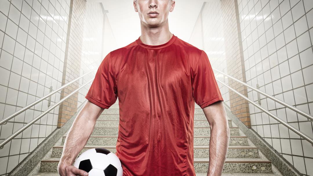 A soccer player wearing a bright red shirt standing on a staircase holding a soccer ball.