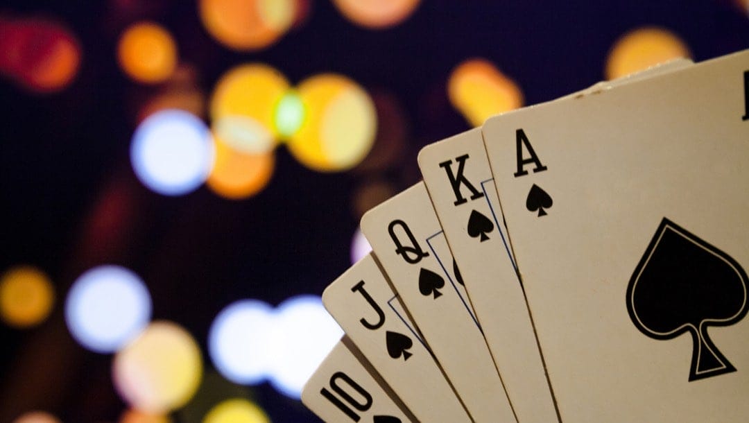 A royal flush in spades with lights in the background.