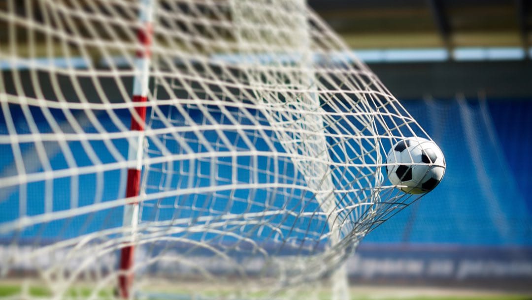A soccer ball going into the net of the goals.