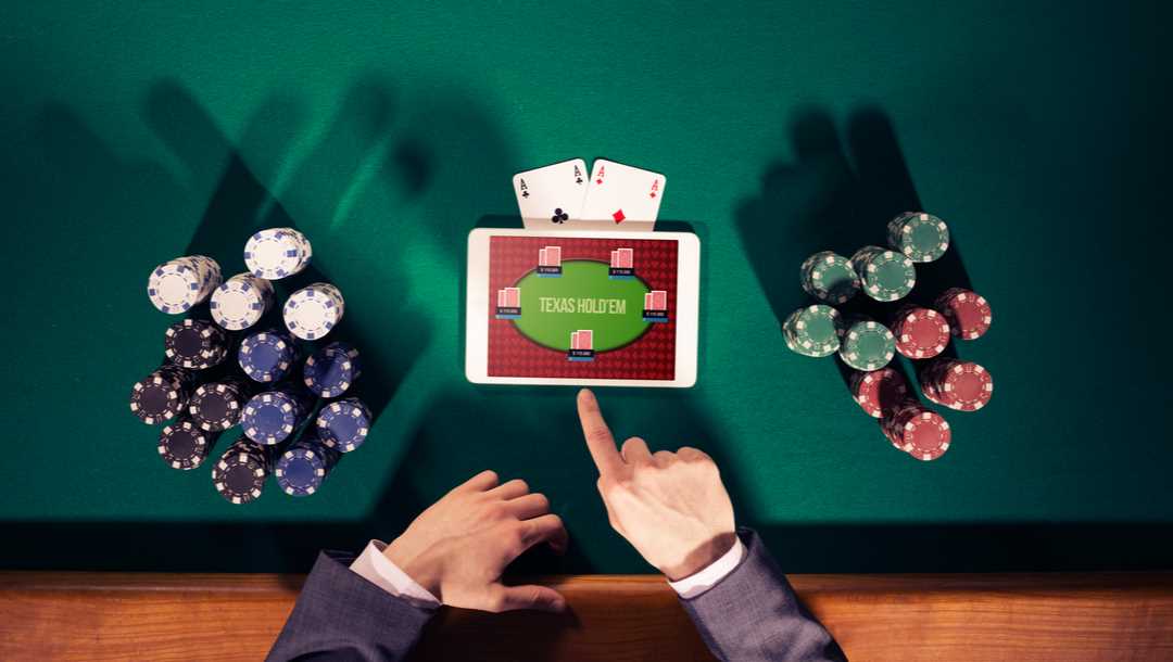 A poker player’s hands point to a digital tablet beside piles of casino chips on a poker table.