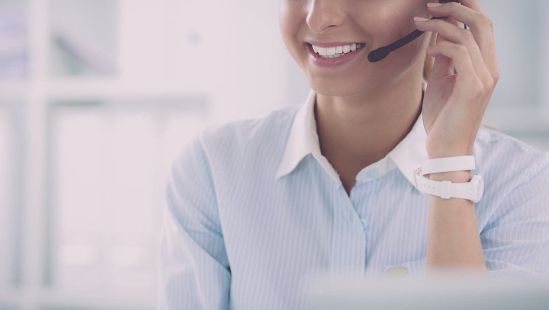 A customer service agent smiling and talking into a headset.
