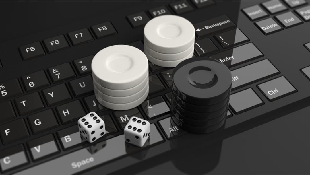 Black and white casino chips and two dice on a shiny black computer keyboard.