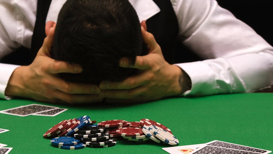 A poker player places his head in his hands on a poker table.