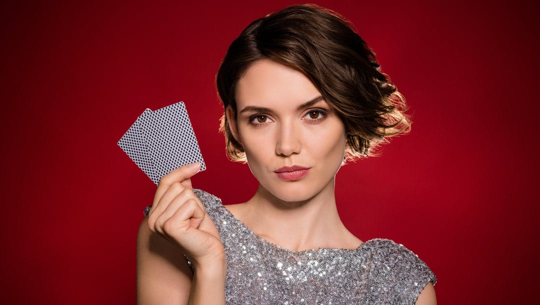 A woman wearing a sequin dress holding two playing cards against a red background.