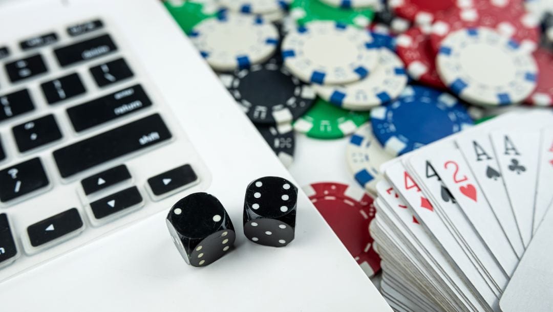 Black dice on a silver laptop with playing cards and casino chips on the right-hand side.
