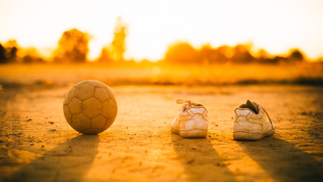 A soccer ball and a pair of children’s shoes in the sunset.