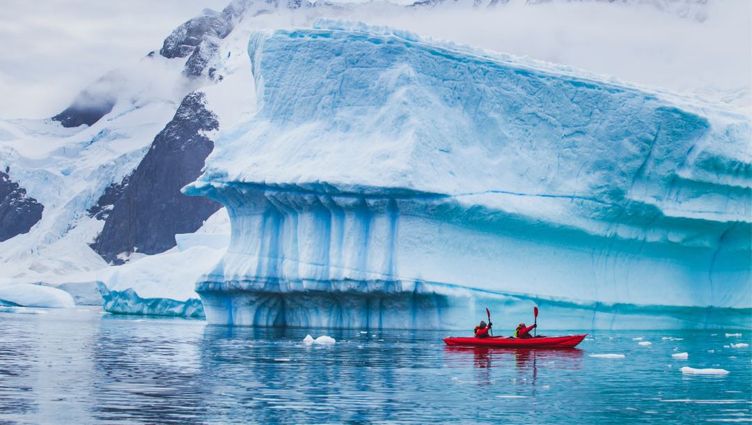 Two people in a red canoe next to a glacier in Antarctica.