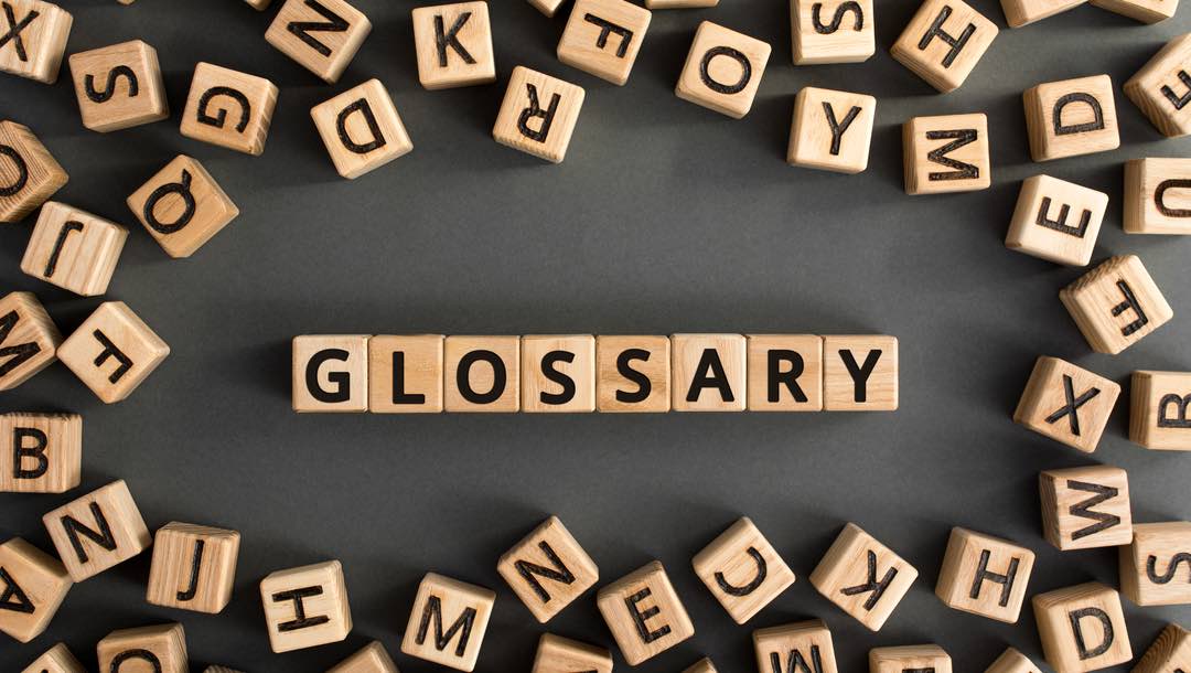 “Glossary” written on wooden blocks surrounded by other letters on a black table.