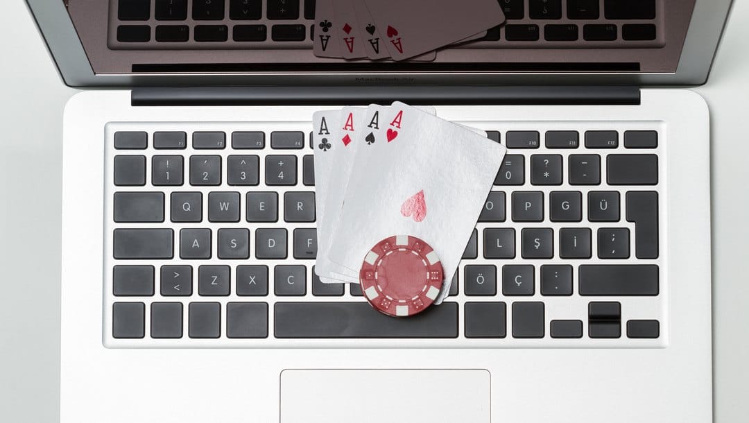 Four aces and a poker chip sit on a laptop keyboard.