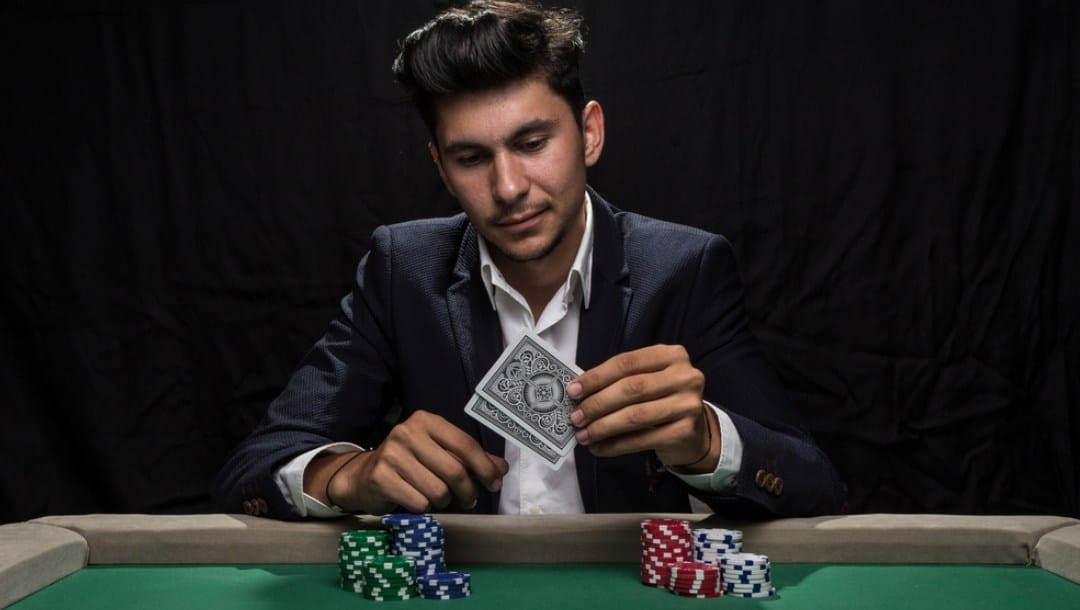 A poker player in a suit lifts his hole cards to check them.