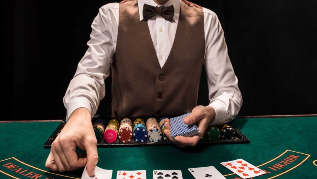 Front view of a casino dealer as they lay out playing cards on a green felt table.