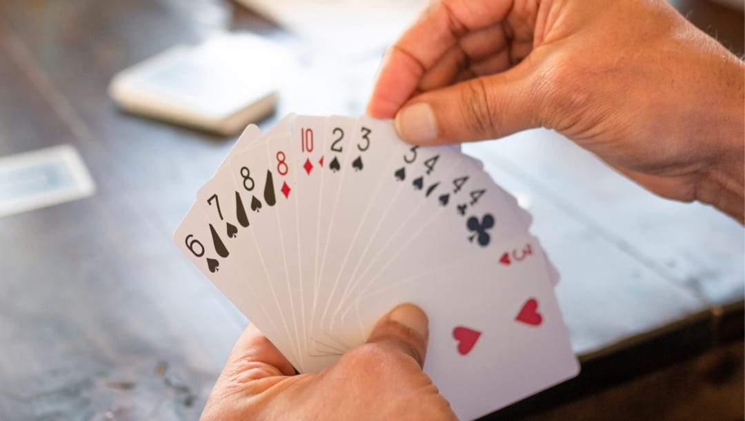 Close-up of a man holding a hand of playing cards during a game of rummy.