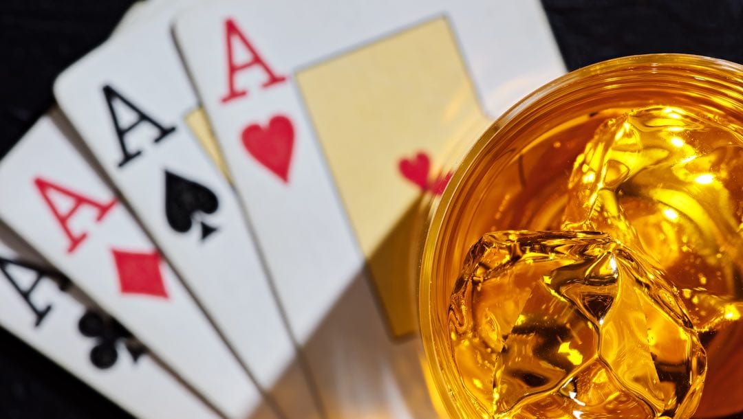 A glass of whiskey on ice and four aces playing cards.