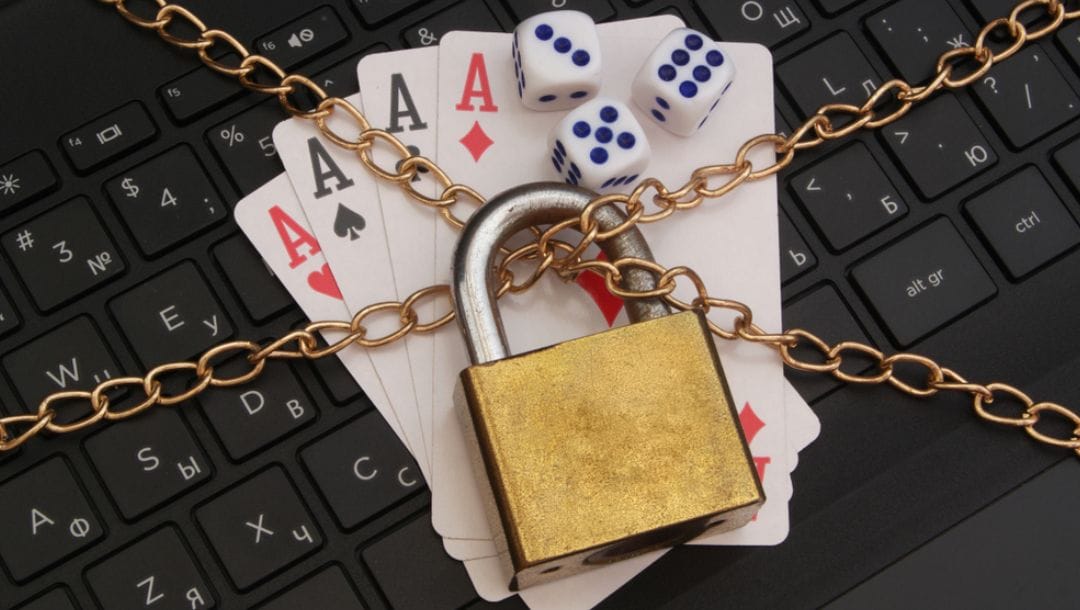 A lock and chain wrapped around a laptop, four aces and a set of three dice.
