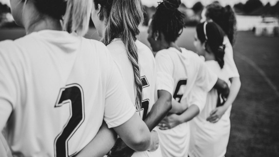 A women’s soccer team huddles together.