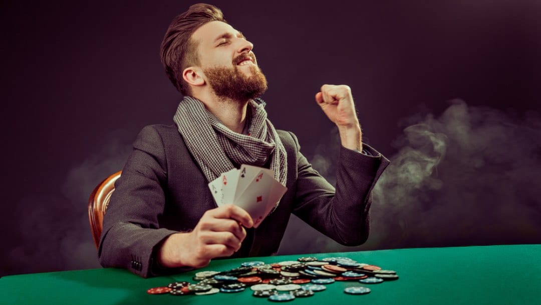 A man at a poker table celebrates having four aces in his hand.