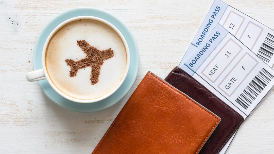 A coffee with airplane art and passport with flight tickets.