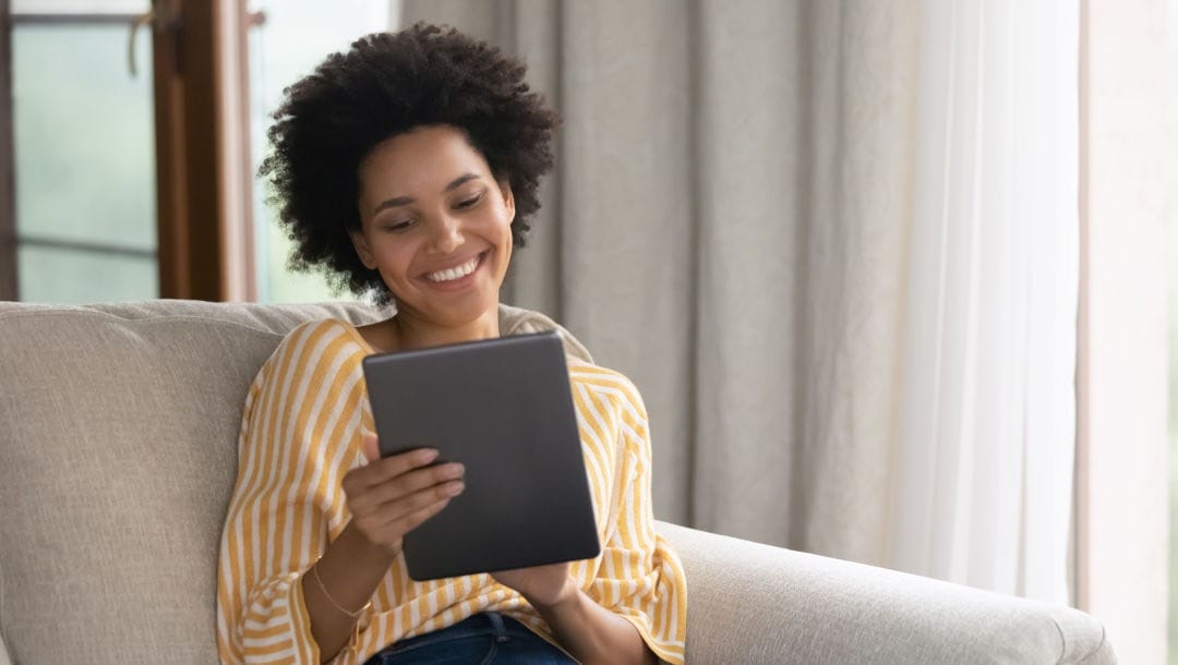 ALT: A woman smiling while looking at a tablet.