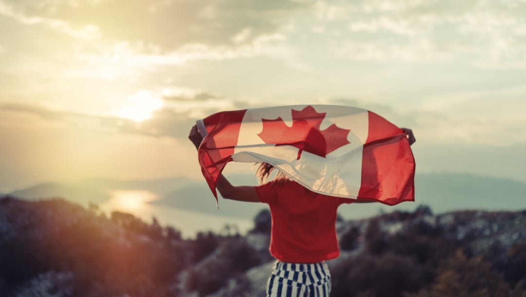 A person standing on a hill in the sunset and holding the Canadian flag.