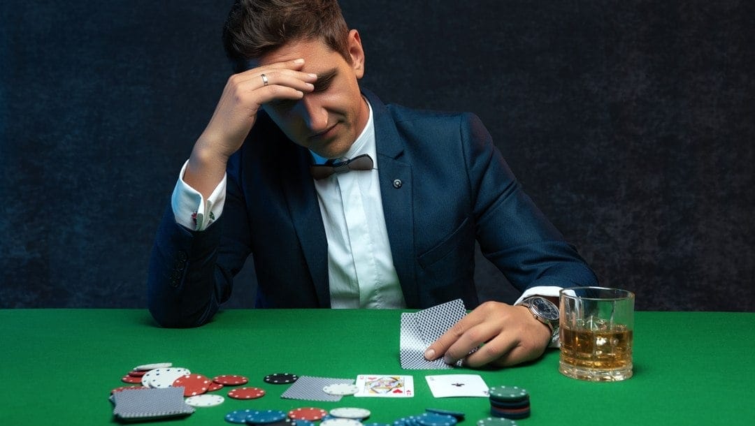 A man at a poker table looks at his hole cards with a concerned look on his face.