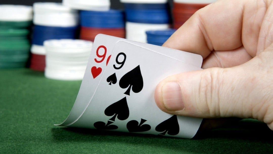 A poker player reveals their hole cards: a pair of nines.