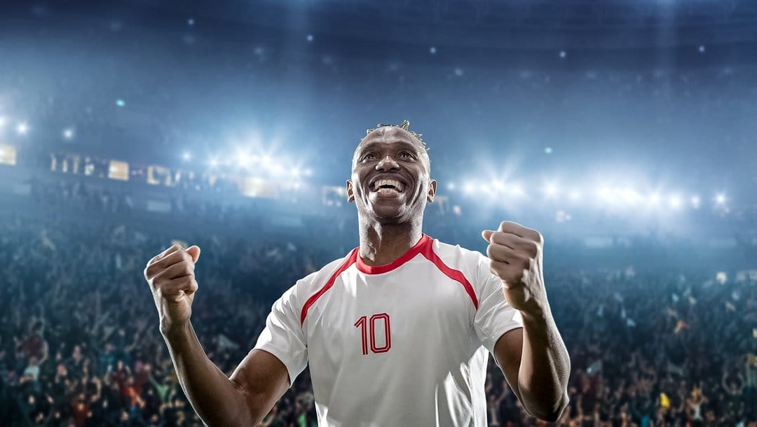A smiling soccer player in a stadium clenches his fists in victory.
