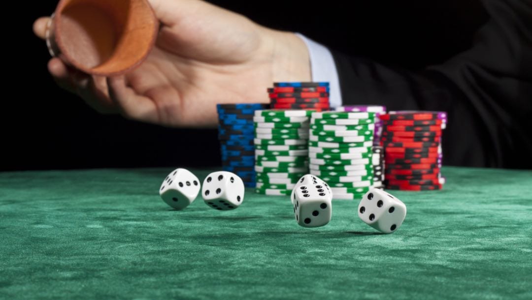A person rolling dice on a poker table.