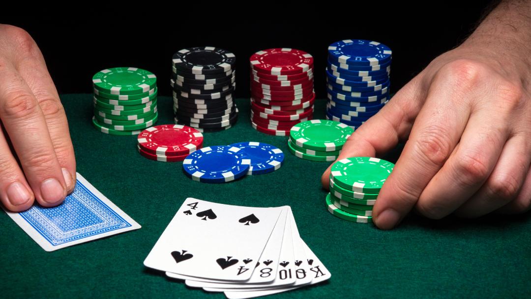 A poker player holds a card in one hand and poker chips in the other.