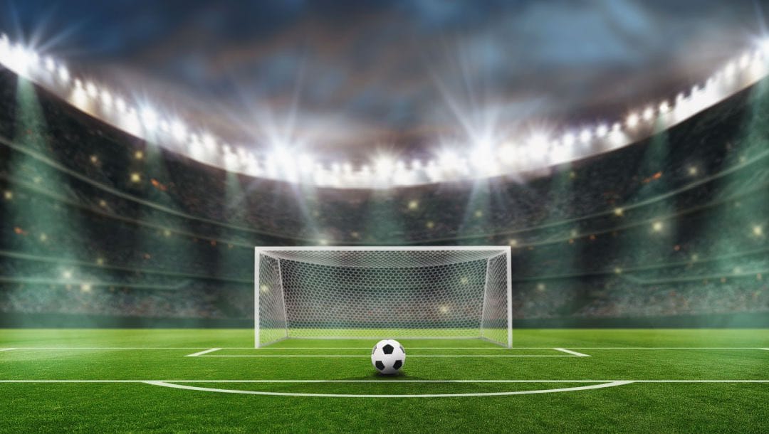A soccer ball positioned in front of a goal post in a large soccer stadium.