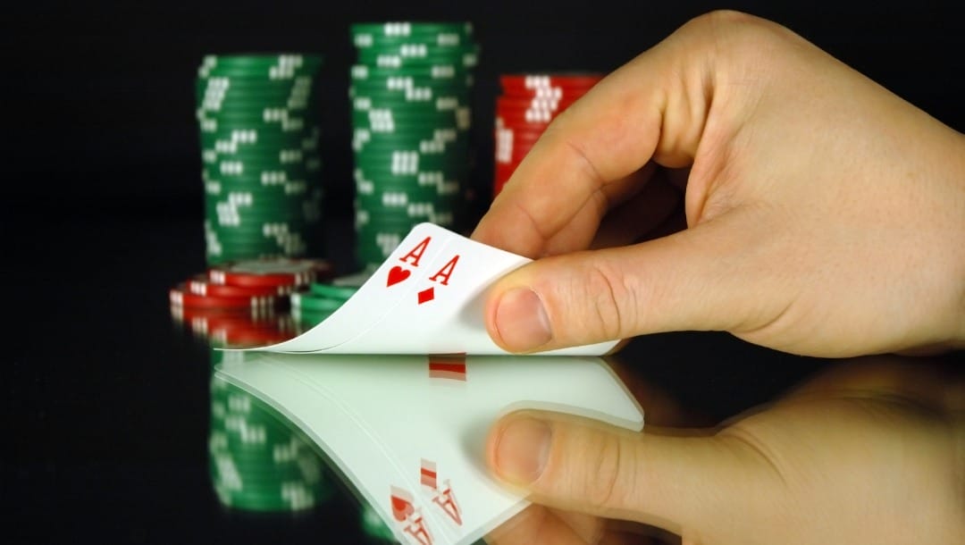 A hand revealing two ace poker cards in front of a stack of casino chips.