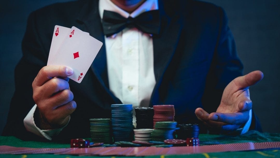 A man at a poker table with chips in front of him shows a pair of aces in his hand.