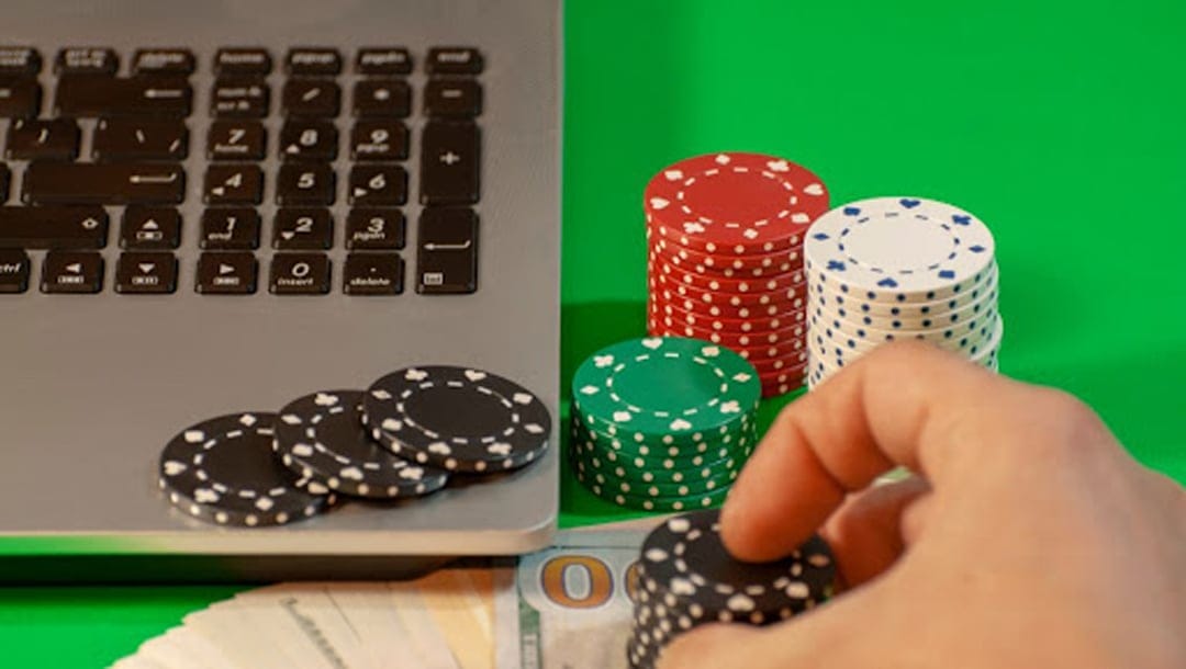 Poker chips and laptop on a green felt table.