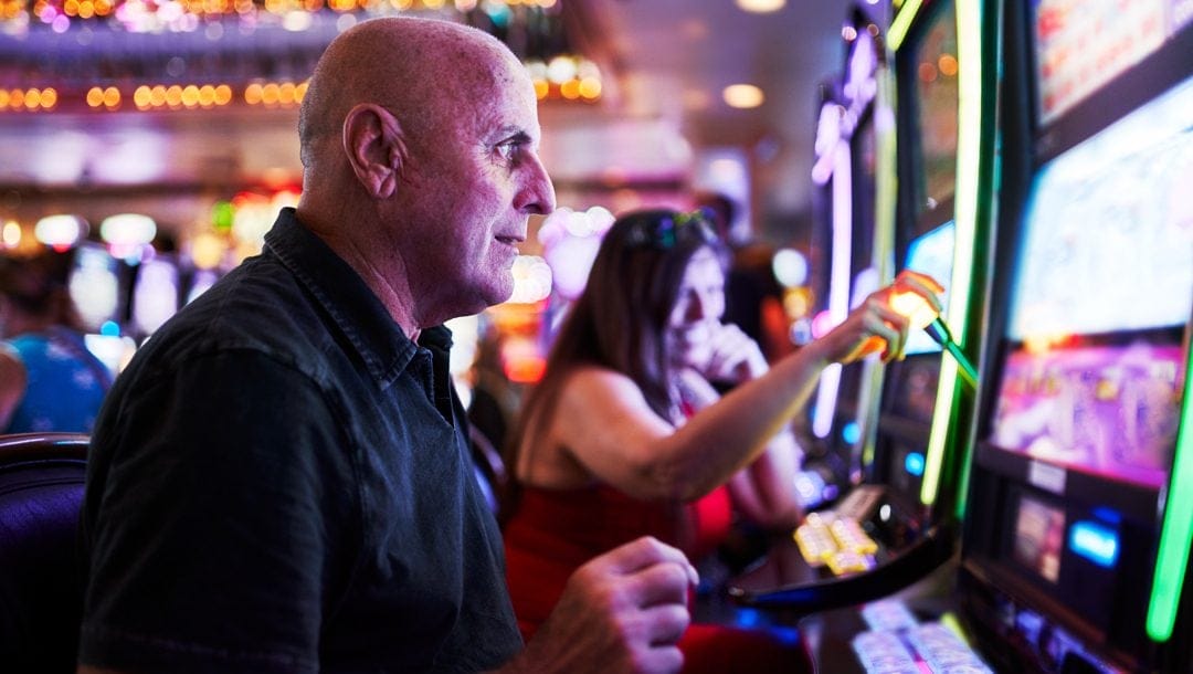 An older person playing at a slot machine in a casino.