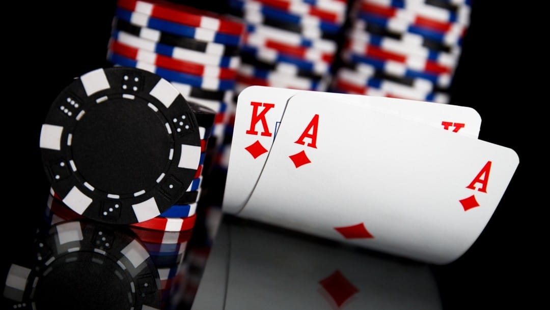 An ace and king hole cards next to stacks of poker chips on a shiny black table.